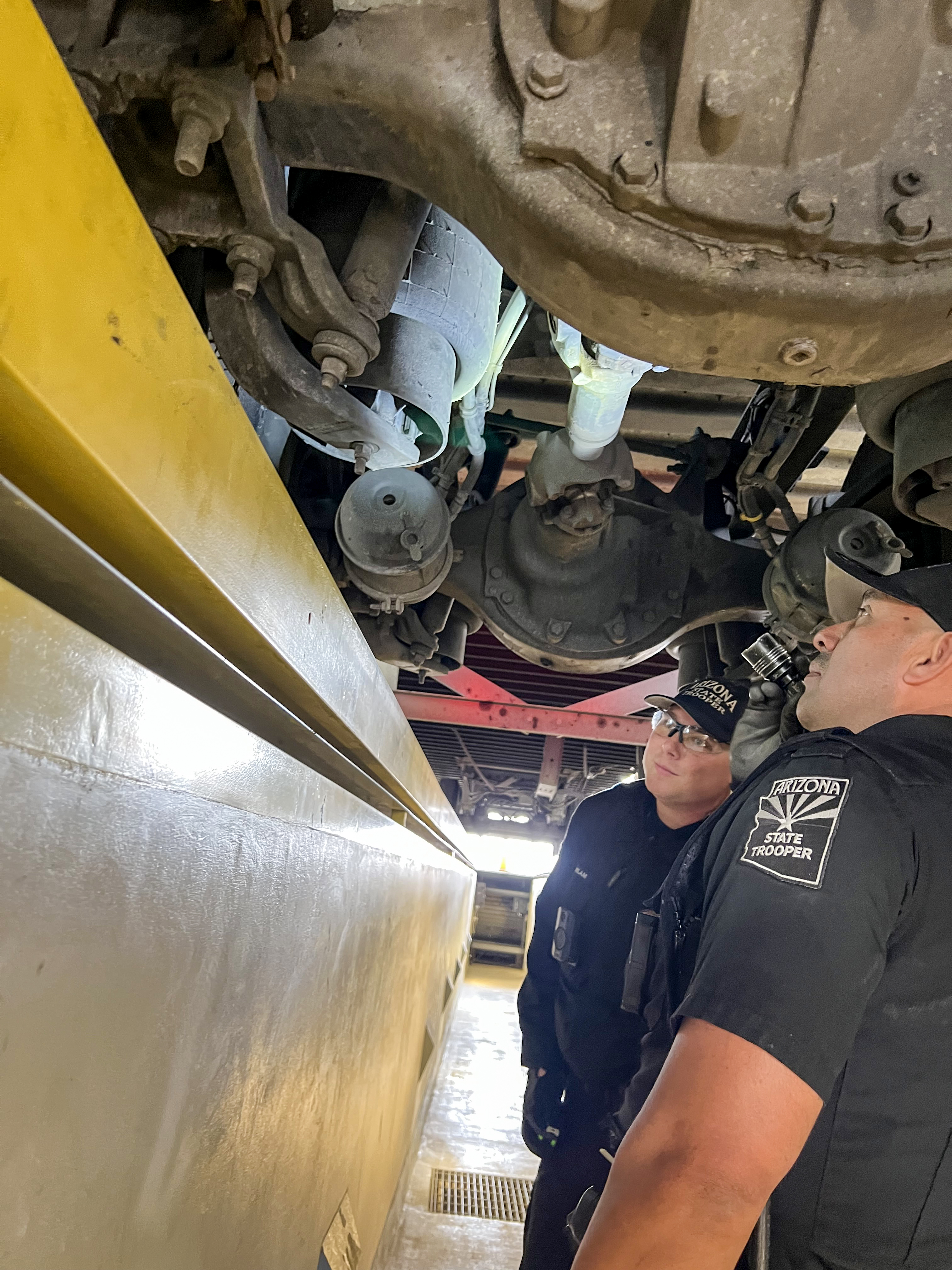 Two CVETF troopers look up at the underside of a semi-truck from an inspection bay