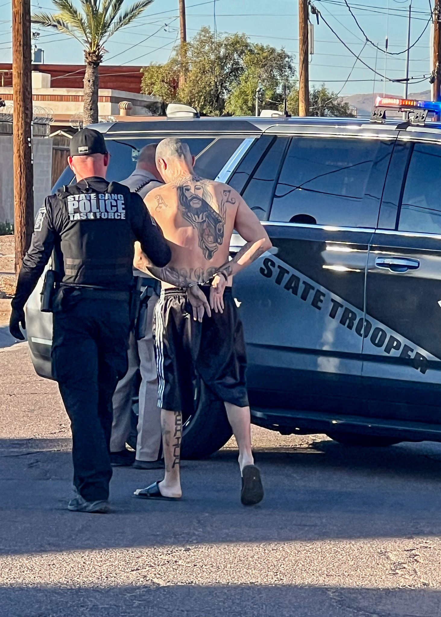 A State Gang Task Force detective escorts a man in handcuffs towards a police vehicle