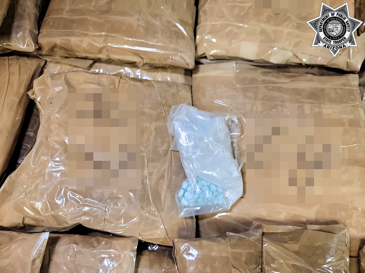 Blue pills in a plastic bag are displayed on top of larger bundles of packages wrapped in brown plastic