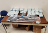 Seized drugs and firearms wrapped in plastic are displayed on a table