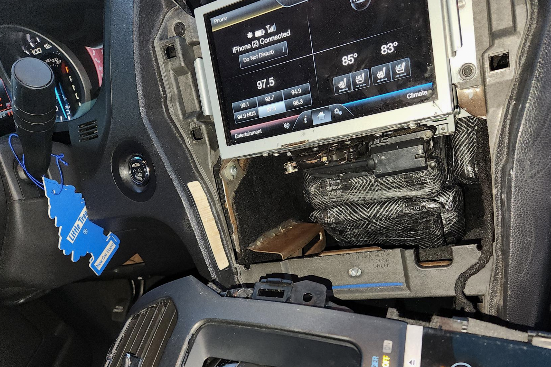 An aftermarket compartment in the dashboard of a car contains plastic wrapped packages 