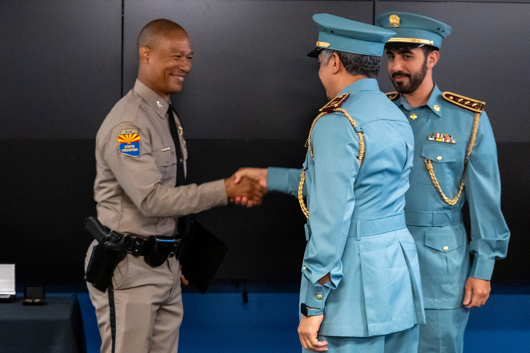 Colonel Glover shakes hands with an ALEAA graduate during the promotion ceremony as Captain Mohamed Alhmoudi looks on.
