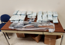 Seized drugs and firearms wrapped in plastic are displayed on a table