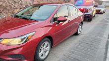A red sedan stopped along the right side of the road with police vehicles behind it