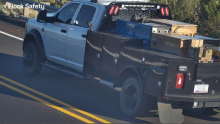 Image of a white Dodge Ram 5500 truck with a black bed and red and blue lights taken from a roadway camera
