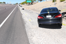 Photo of the crash scene along I-10 showing a damaged black Mercedes sedan pushed off the right shoulder and a damaged white car stopped farther down the scene.