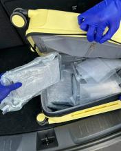 Plastic wrapped packages of cocaine are visible inside a partially open yellow rolling suitcase