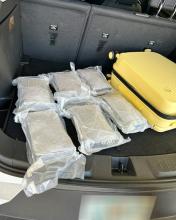 Plastic wrapped packages of cocaine are visible inside a partially open yellow rolling suitacse
