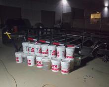 Photograph of 21 five-gallon buckets filled with liquid methamphetamine beside the F350 truck and trailer.