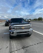 A gray Chevrolet pickup truck stopped on the shoulder of a highway with AZDPS vehicles behind it.