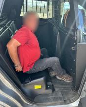 A man in handcuffs in the back of an AZDPS patrol vehicle. His face is blurred.