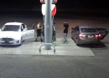 Screenshot from a gas station camera showing two cars parked at gas pumps. Three males are at the gas pumps.