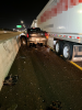 Rear view of a crashed white tractor-trailer stuck in the median wall with a dark pickup truck stuck beside it