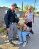  A small tan dog sits in the lap of man in a folding chair while a SWAT trooper and another man look on and smile
